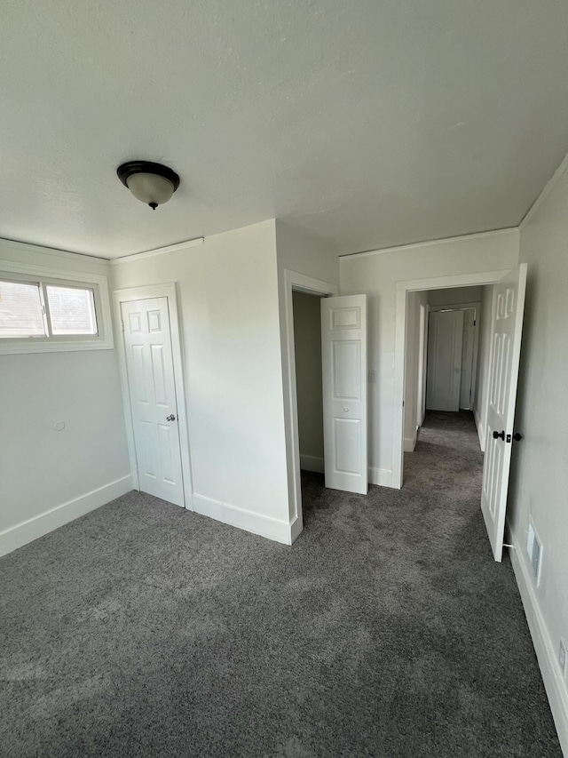 spare room featuring dark carpet, visible vents, and baseboards