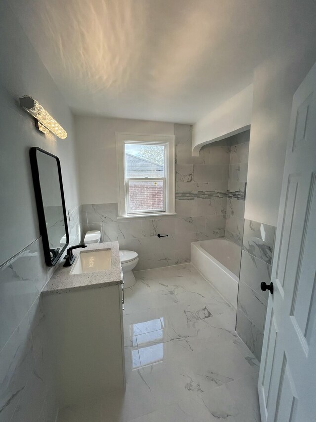 bathroom with a bathing tub, vanity, tile walls, marble finish floor, and toilet