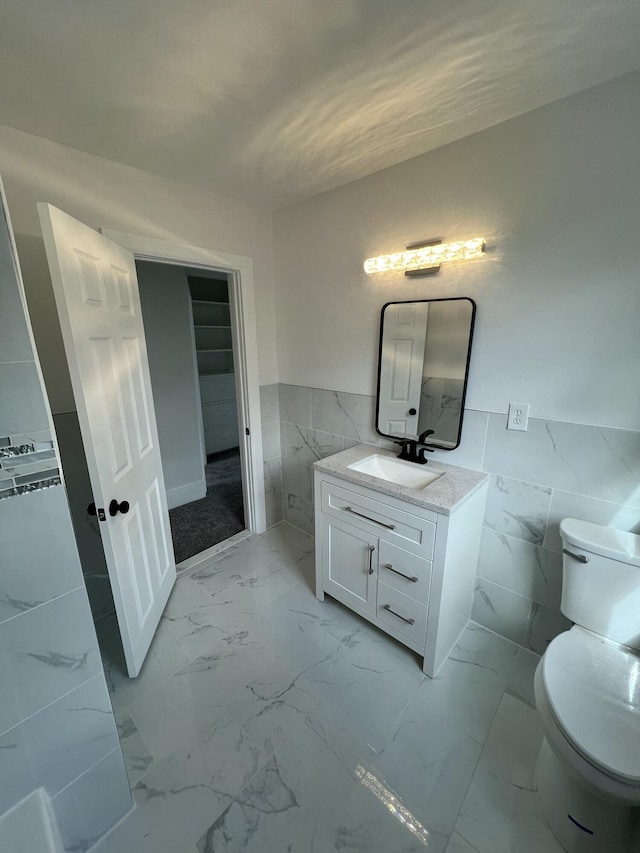 bathroom with a wainscoted wall, toilet, tile walls, marble finish floor, and vanity