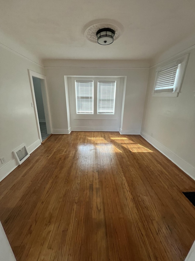 empty room with plenty of natural light, visible vents, and wood finished floors