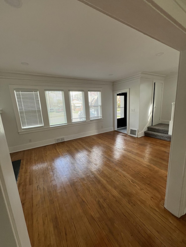 unfurnished living room featuring stairway, baseboards, crown molding, and visible vents