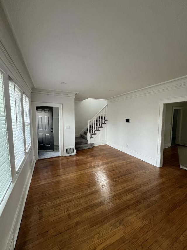 unfurnished living room with stairway, visible vents, baseboards, and wood finished floors
