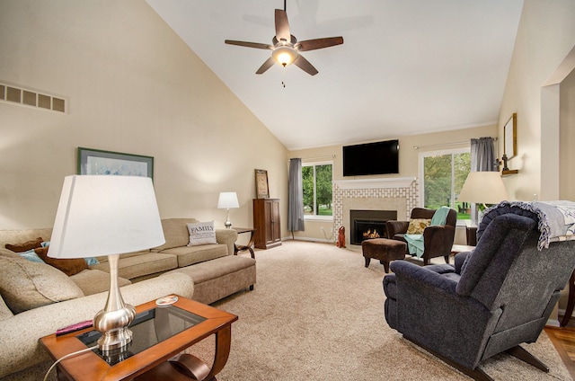 living room with ceiling fan, a lit fireplace, light colored carpet, visible vents, and high vaulted ceiling