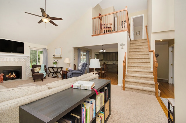 carpeted living room with a tile fireplace, wood finished floors, stairway, high vaulted ceiling, and ceiling fan with notable chandelier