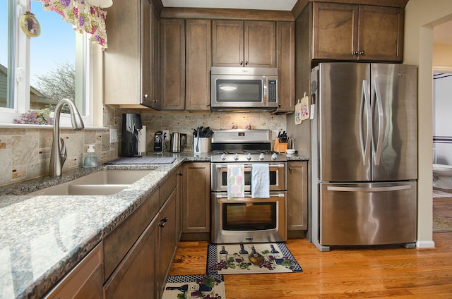 kitchen with tasteful backsplash, a sink, light stone counters, light wood-style floors, and stainless steel appliances