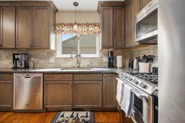 kitchen with stainless steel appliances, a sink, light wood finished floors, and tasteful backsplash