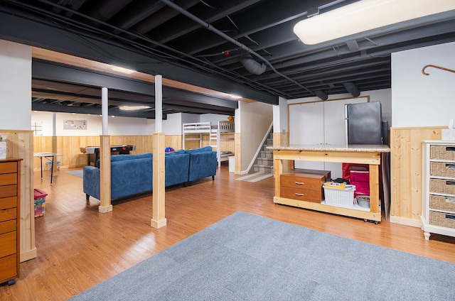 finished below grade area with light wood-style floors, wainscoting, and wood walls
