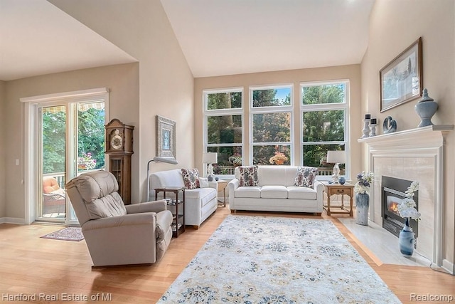 living area with lofted ceiling, a tiled fireplace, baseboards, and light wood finished floors