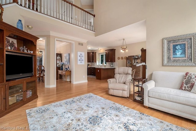 living room with baseboards, a towering ceiling, visible vents, and light wood-type flooring