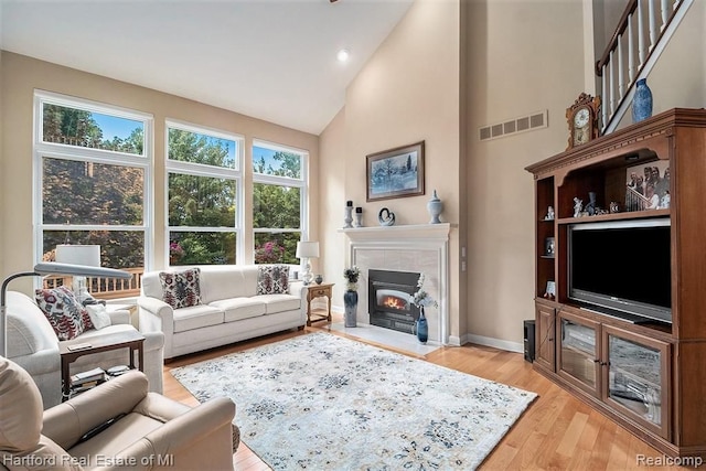 living room with high vaulted ceiling, light wood-style floors, a fireplace with flush hearth, baseboards, and visible vents