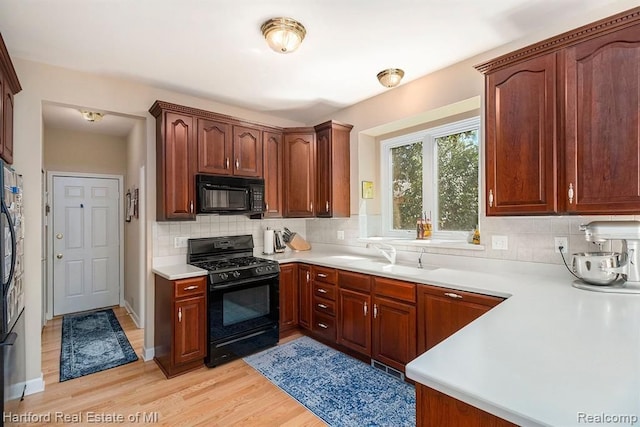 kitchen with backsplash, light wood-type flooring, a sink, and black appliances