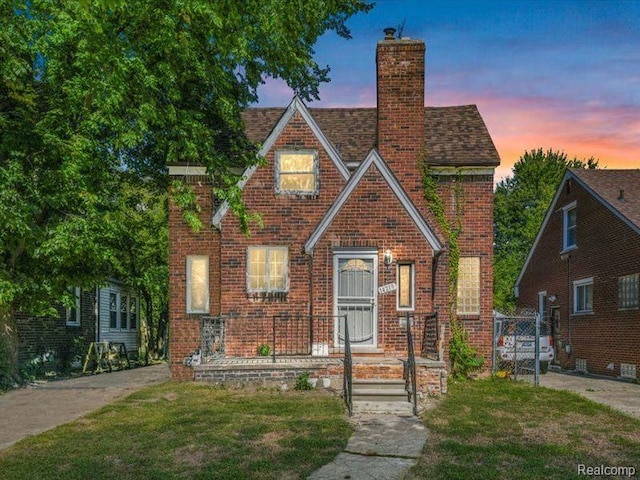 tudor house featuring a chimney, brick siding, and a front yard