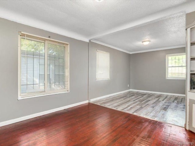 spare room featuring baseboards, ornamental molding, wood finished floors, and a textured ceiling