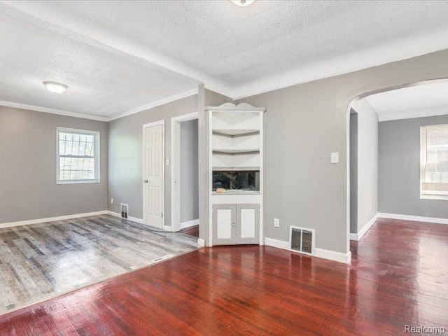 unfurnished living room featuring arched walkways, wood finished floors, visible vents, and a textured ceiling
