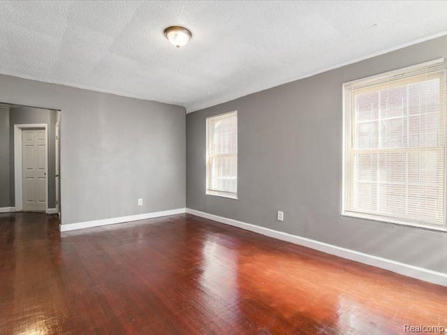 empty room with baseboards, a textured ceiling, and dark wood-style floors