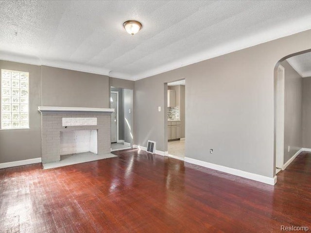 unfurnished living room with visible vents, a fireplace, wood finished floors, and arched walkways