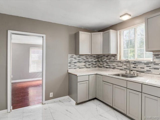 kitchen featuring marble finish floor, baseboards, gray cabinetry, and a sink