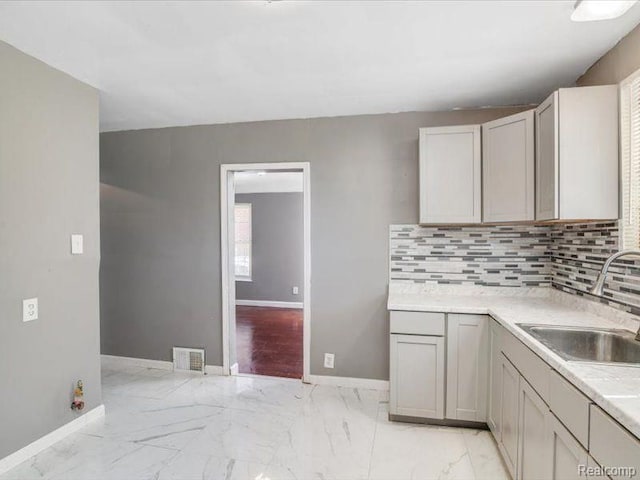 kitchen with baseboards, visible vents, a sink, and tasteful backsplash