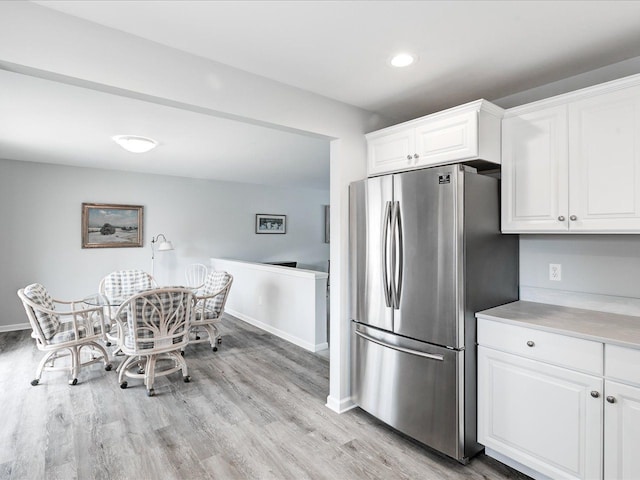kitchen featuring light wood-style flooring, freestanding refrigerator, light countertops, white cabinets, and baseboards