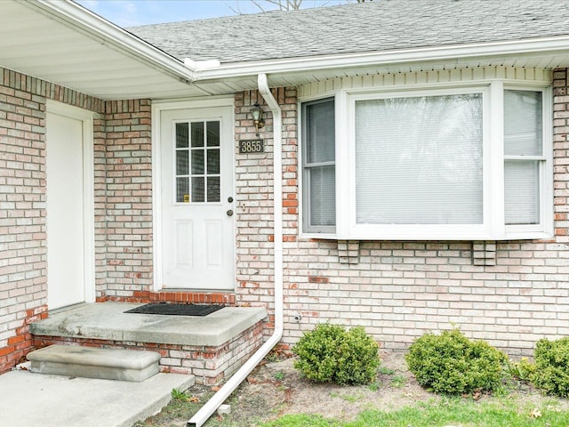 property entrance featuring brick siding and a shingled roof