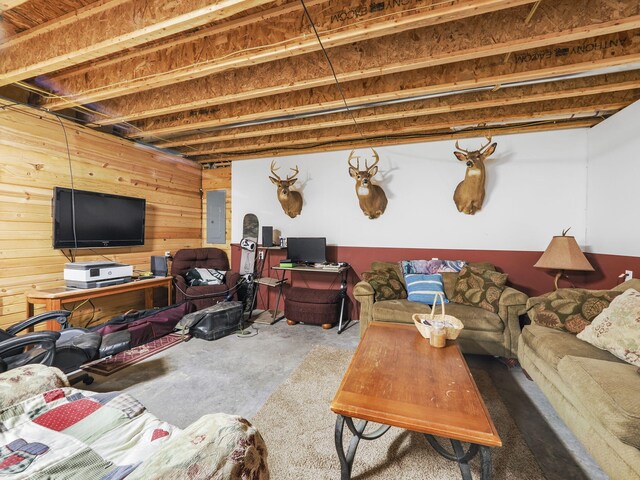 living area featuring wooden walls, electric panel, and unfinished concrete flooring