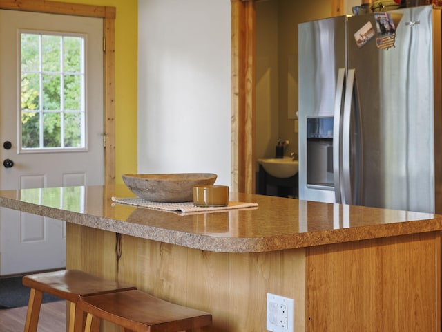 kitchen with wood finished floors, stainless steel refrigerator with ice dispenser, and a kitchen breakfast bar
