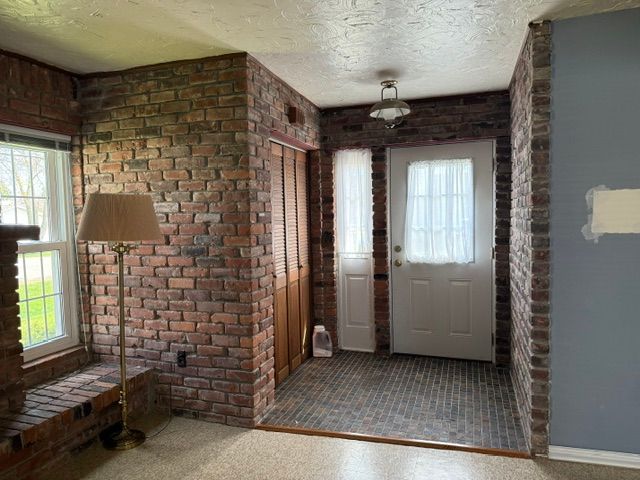 entryway with brick wall, a wealth of natural light, and a textured ceiling