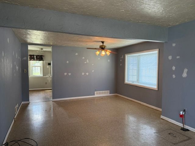 empty room with ceiling fan, baseboards, tile patterned floors, and a textured ceiling