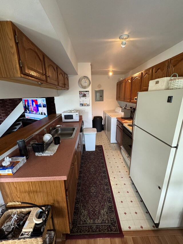 kitchen with a sink, electric panel, light floors, white appliances, and washer / dryer