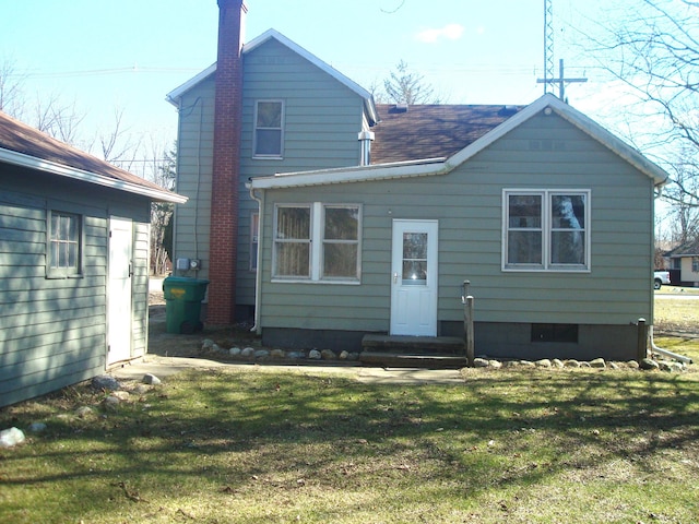 rear view of house with a lawn, a shingled roof, a chimney, and entry steps