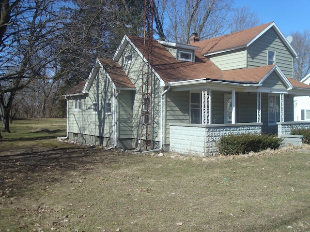 view of side of home featuring a yard, a chimney, and covered porch