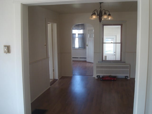 interior space featuring arched walkways, radiator, a chandelier, baseboard heating, and wood finished floors