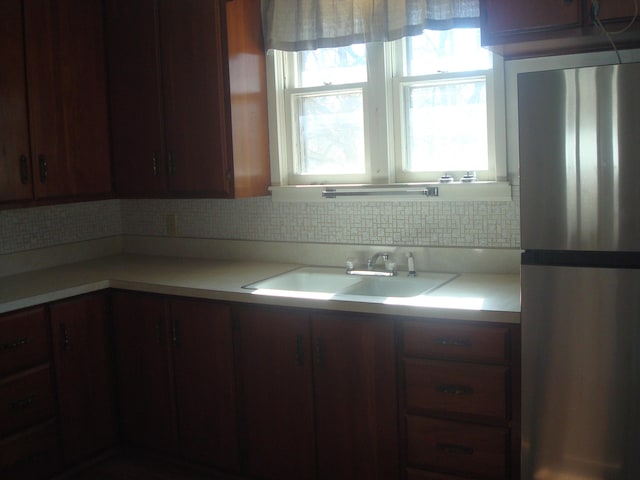 kitchen featuring light countertops, freestanding refrigerator, tasteful backsplash, and a sink