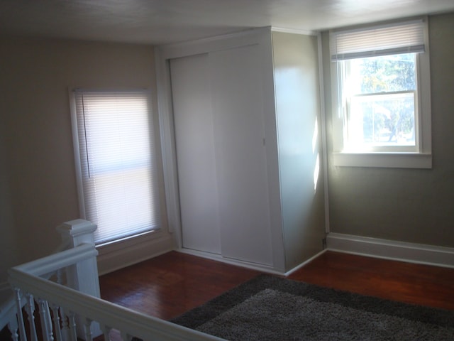 unfurnished bedroom featuring multiple windows, baseboards, a closet, and dark wood-style flooring