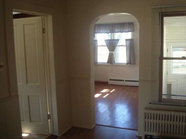 spare room with radiator, arched walkways, wood finished floors, and a baseboard radiator