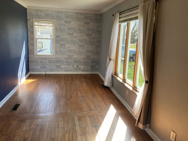 empty room featuring an accent wall, visible vents, baseboards, and a wealth of natural light