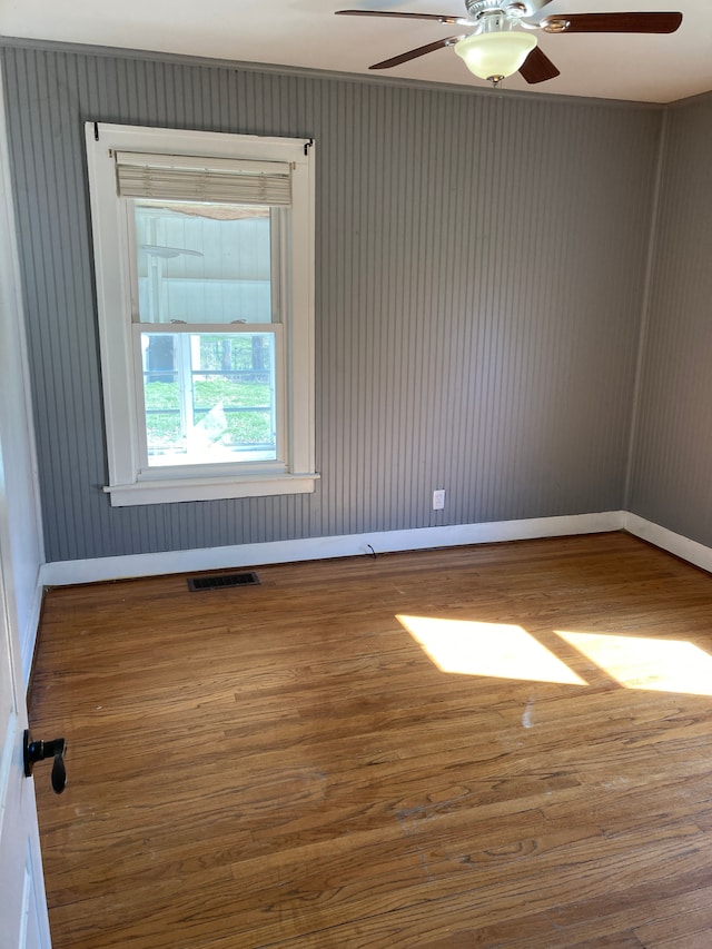 spare room with wood finished floors, visible vents, baseboards, and ceiling fan