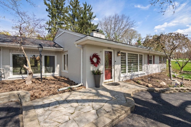 ranch-style home featuring a chimney, brick siding, and a patio