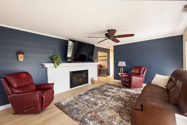 living room with a glass covered fireplace, a ceiling fan, baseboards, ornamental molding, and wood finished floors