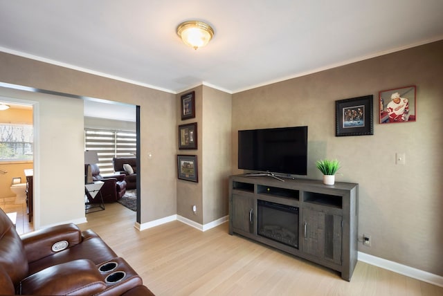 living room with a glass covered fireplace, light wood-style floors, ornamental molding, and baseboards