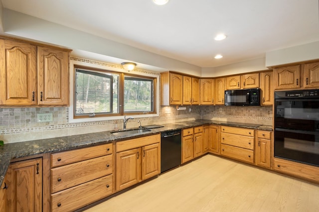 kitchen with dark stone counters, brown cabinetry, light wood-style floors, black appliances, and a sink