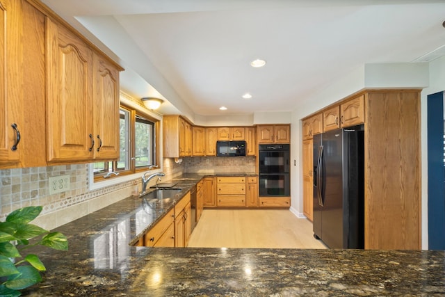 kitchen featuring a sink, light wood-style floors, dark stone countertops, tasteful backsplash, and black appliances