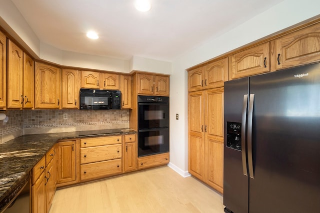 kitchen with dark stone counters, brown cabinets, tasteful backsplash, light wood-style flooring, and black appliances