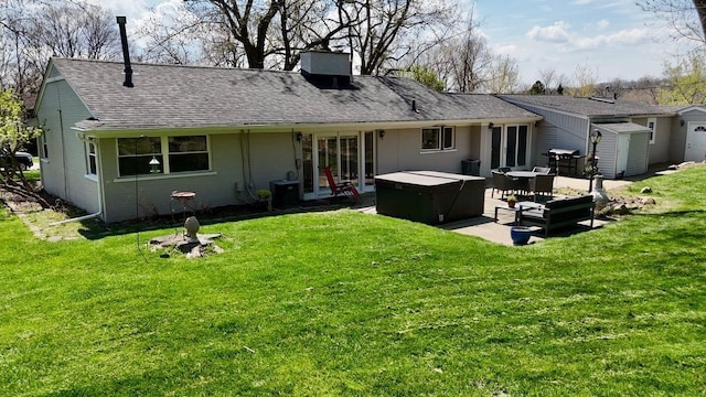rear view of property featuring a hot tub, a patio, roof with shingles, a shed, and a lawn