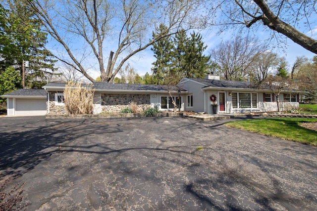 single story home featuring a chimney, driveway, and stone siding