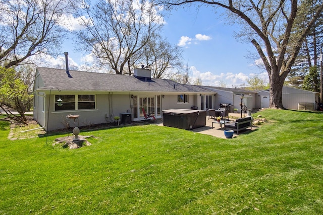 back of house with a yard, a chimney, a patio area, and a hot tub