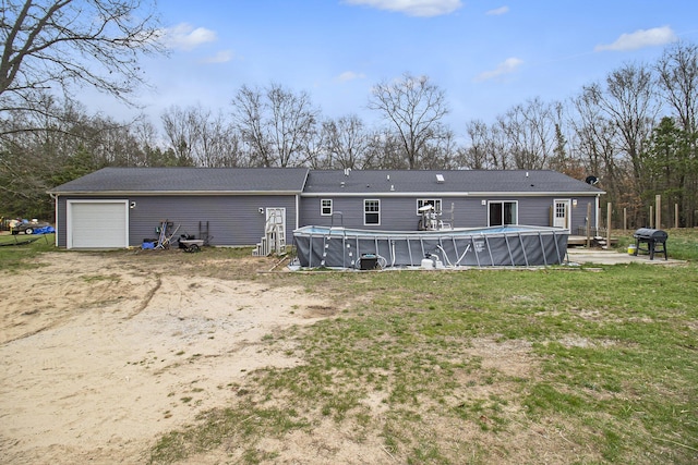 rear view of house with driveway, an outdoor pool, a yard, and a garage