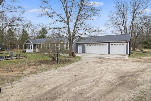 ranch-style house with a detached garage, a trampoline, dirt driveway, and a front lawn