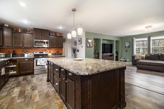 kitchen with stainless steel appliances, a center island, dark brown cabinets, open floor plan, and light stone countertops