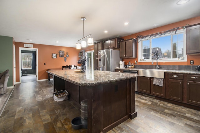kitchen with stainless steel appliances, a sink, dark wood-type flooring, a center island, and dark brown cabinetry
